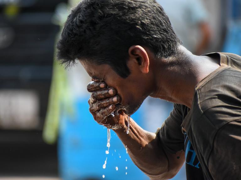 Ein indischer Mann spritzt sich mit der rechten Hand Wasser ins Gesicht.