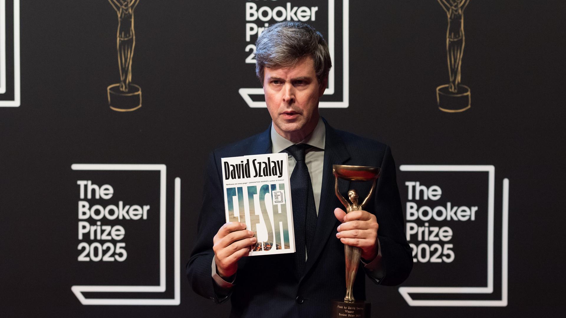 David Szalay hält sein Buch und die Trophäe des Booker Prize in der Hand