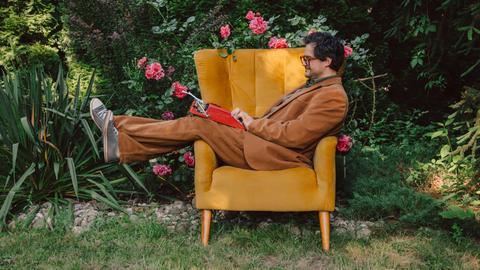 Ein Mann im Anzug liegt im Garten auf einem Sessel und tippt auf einer Schreibmaschine