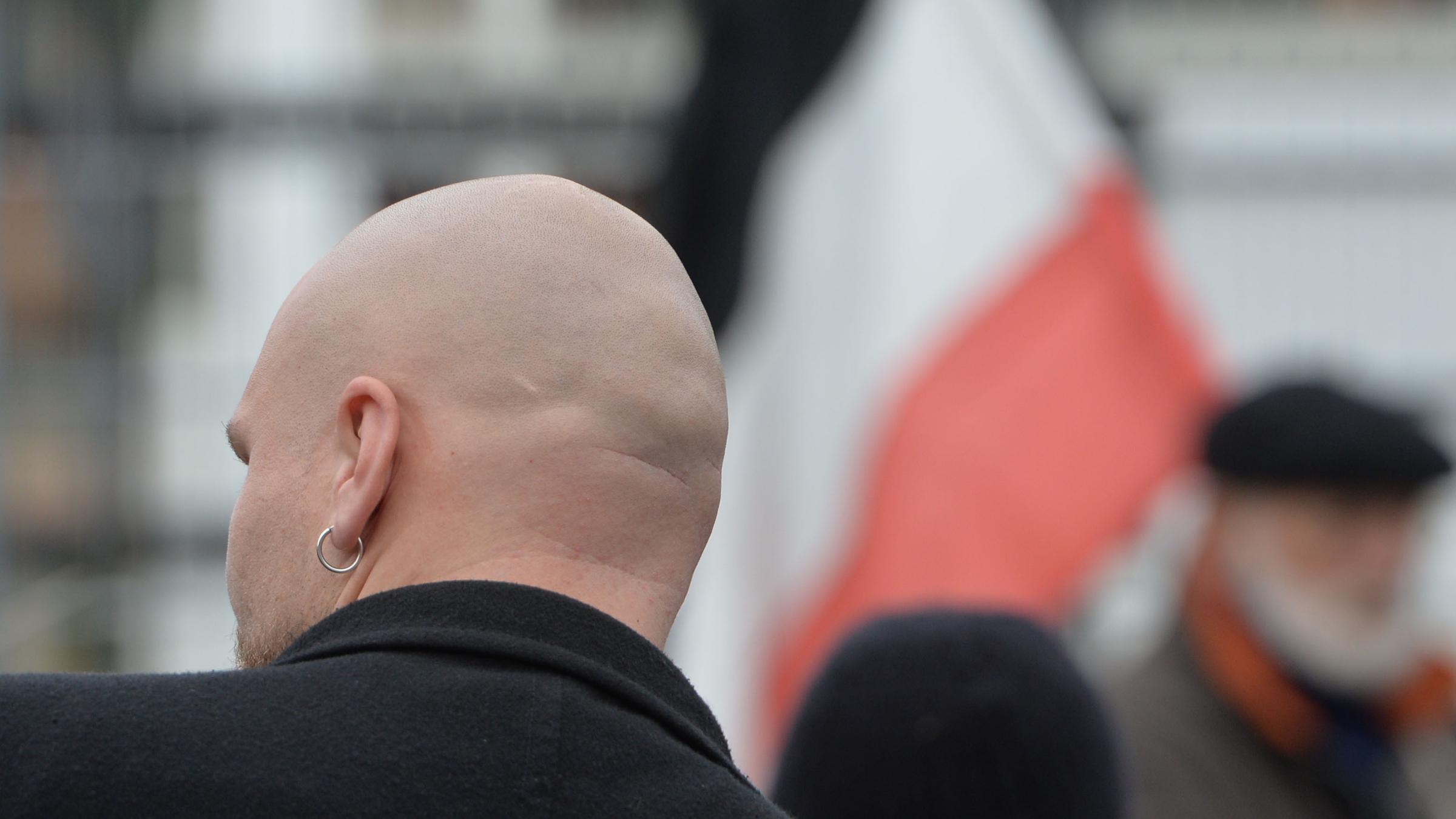 Von hinten ein glatzköpfiger Teilnehmer eines Neonazi-Aufmarsches mit schwarzer Bomberjacke. Im Hintergrund die Reichsflagge.