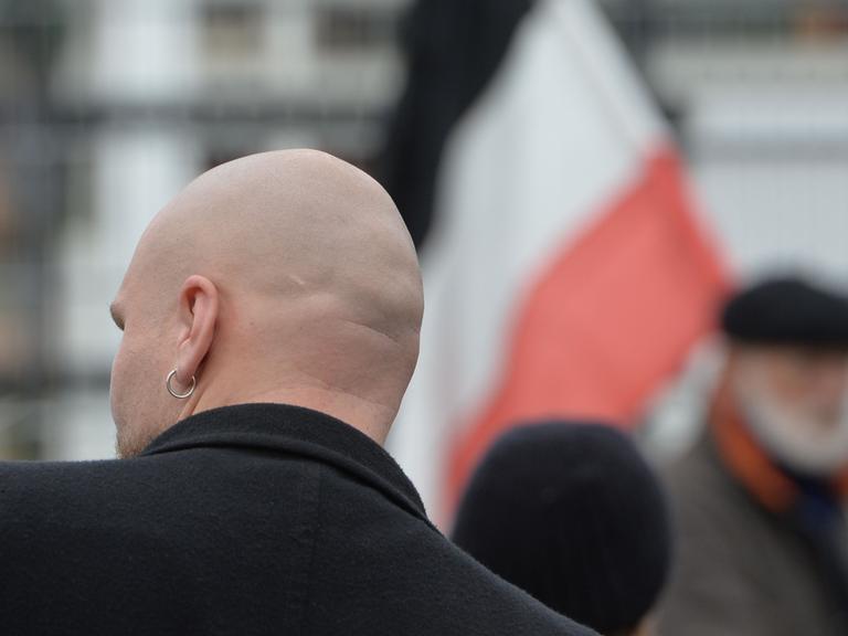 Von hinten ein glatzköpfiger Teilnehmer eines Neonazi-Aufmarsches mit schwarzer Bomberjacke. Im Hintergrund die Reichsflagge.