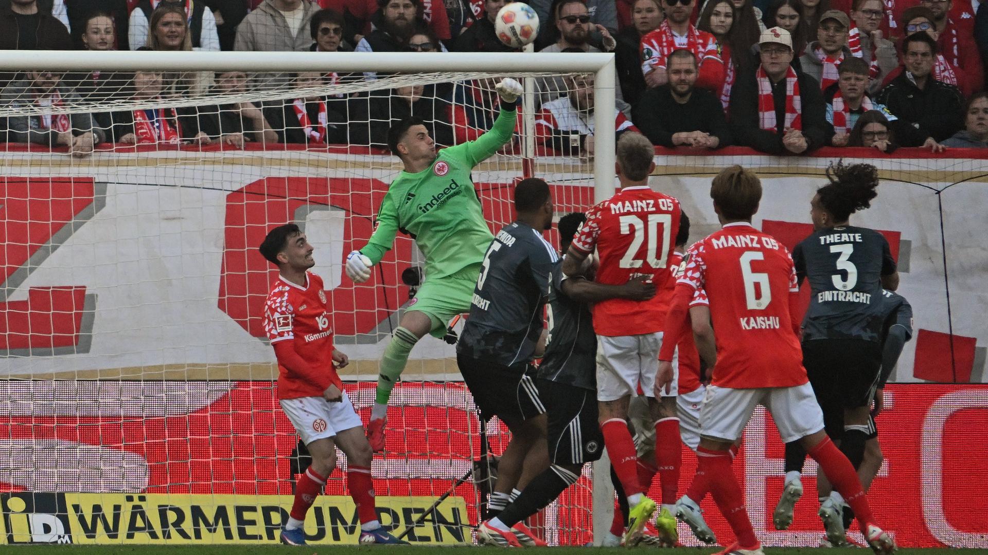 Torhüter Michael Zetterer von Eintracht Frankfurt klärt den Ball in seinem Strafraum. Dort sind drei rot-gekleidete Mainzer Spieler und drei verteidigende Frankfurter Spieler in schwarzen Trikots. Torhüter Michael Zetterer von Eintracht Frankfurt klärt den Ball in seinem Strafraum. Dort sind drei rot-gekleidete Mainzer Spieler und drei verteidigende Frankfurter Spieler in schwarzen Trikots.