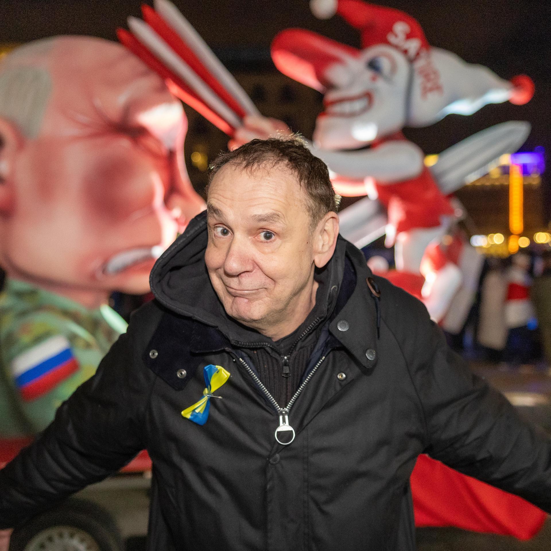 Tilly steht vor dem Wagen und breitet mit spöttischem Lächeln beide Arme aus. Es ist dunkel. Dahinter der Wagen, in dem eine Putin-Figur den Düsseldorfer Schalk "Hoppeditz" mit einem Schwert aufspießt. Dieser schlägt Putin mit einer Klatsche auf den Kopf.