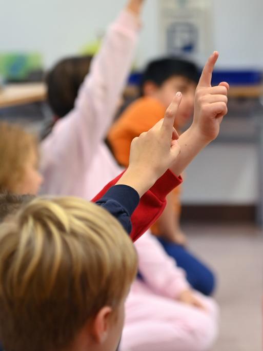 Grundschülerinnen und Grundschüler melden sich im Unterricht. 