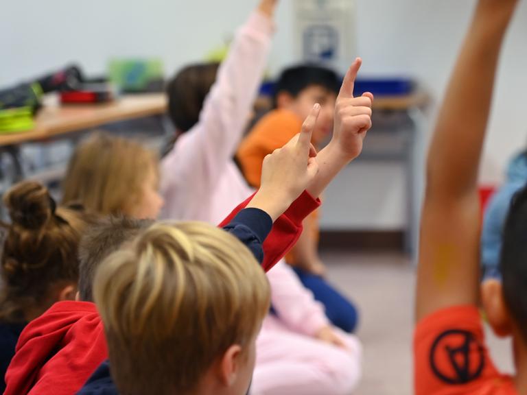 Grundschülerinnen und Grundschüler melden sich im Unterricht. 