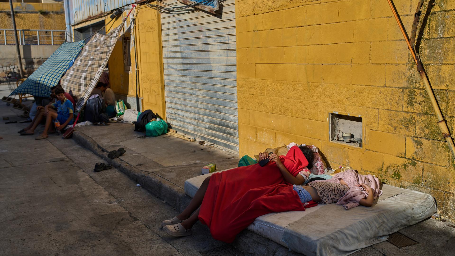 Migranten, die von Marokko nach Spanien eingereist sind, schlafen unter Decken auf der Straße vor einem Lagerhausgelände nahe der spanisch-marokkanischen Grenze in der spanischen Enklave Ceuta. Migranten, die von Marokko nach Spanien eingereist sind, schlafen unter Decken auf der Straße vor einem Lagerhausgelände nahe der spanisch-marokkanischen Grenze in der spanischen Enklave Ceuta.