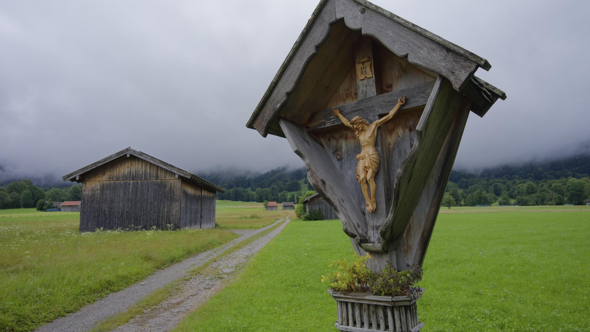 Ein Wegkreuz steht an einem Wanderpfad, im Hintergrund liegt der Wald im Nebel. Ein Wegkreuz steht an einem Wanderpfad, im Hintergrund liegt der Wald im Nebel.