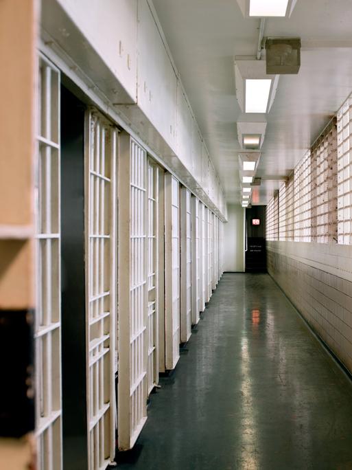 Blick in einen Zellengang im Gefängnis. Die Fenster auf der rechten Seite sind vergittert. Links sind die Zellentüren zu sehen.