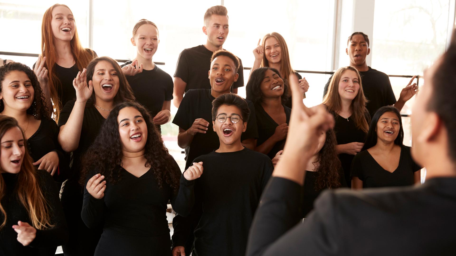 Menschen singen in einem Chor, der von einem Chorleiter dirigiert wird. Menschen singen in einem Chor, der von einem Chorleiter dirigiert wird.