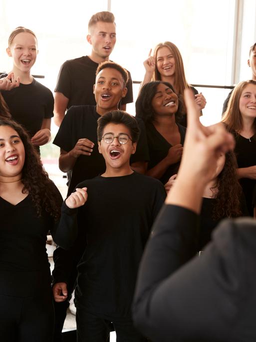 Menschen singen in einem Chor, der von einem Chorleiter dirigiert wird. Menschen singen in einem Chor, der von einem Chorleiter dirigiert wird.