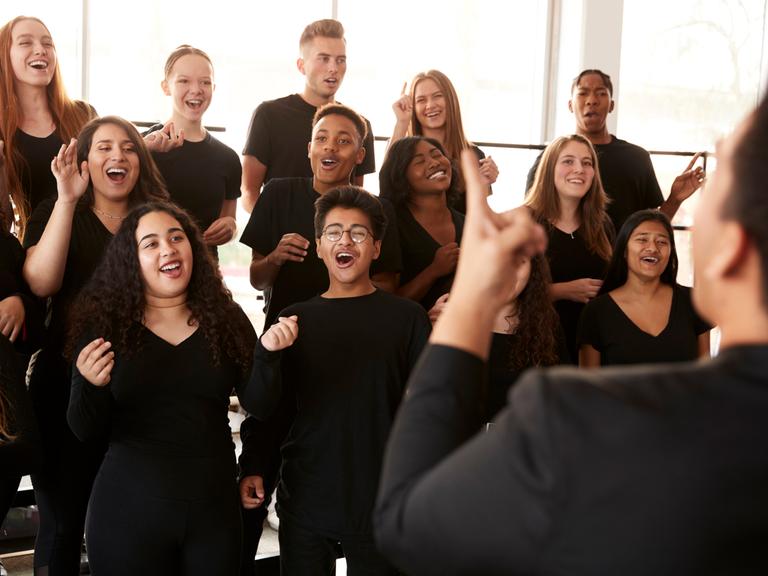Menschen singen in einem Chor, der von einem Chorleiter dirigiert wird. Menschen singen in einem Chor, der von einem Chorleiter dirigiert wird.