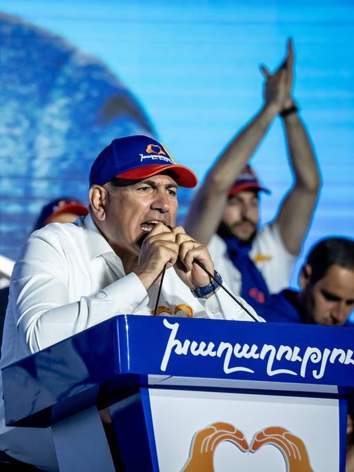 Der Regierungschef von Armenien, Nikol Paschinjan, steht mit Basecap an einem Rednerpult und spricht leidenschaftlich