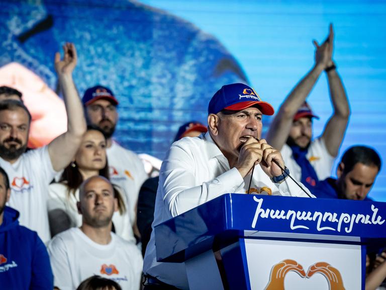 Der Regierungschef von Armenien, Nikol Paschinjan, steht mit Basecap an einem Rednerpult und spricht leidenschaftlich