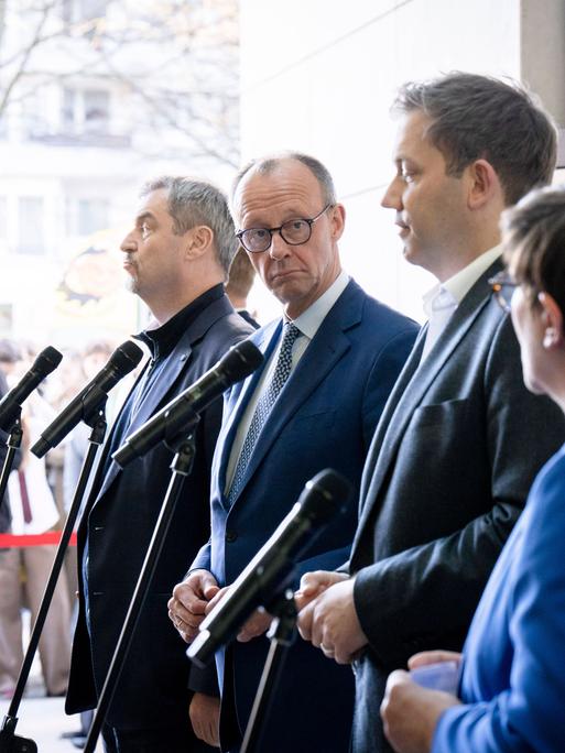 Markus Söder, Friedrich Merz, Lars Klingbeil und Saskia Esken stehen bei einer Pressekonferenz vor den Mikrofonen. Friedrich Merz schaut seitlich in die Kamera. 