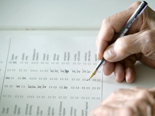 Eine Hand hält einen Kugeschreiber und kreuzt auf einem Fragebogen Antwortmöglichkeiten an.