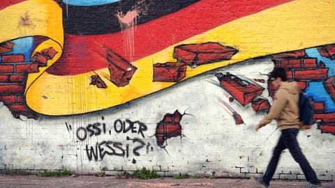 Ein Passant geht in Berlin an an einem Wandbild mit der deutschen Nationalflagge und dem Schriftzug "Ossi oder Wessi? vorbei. 