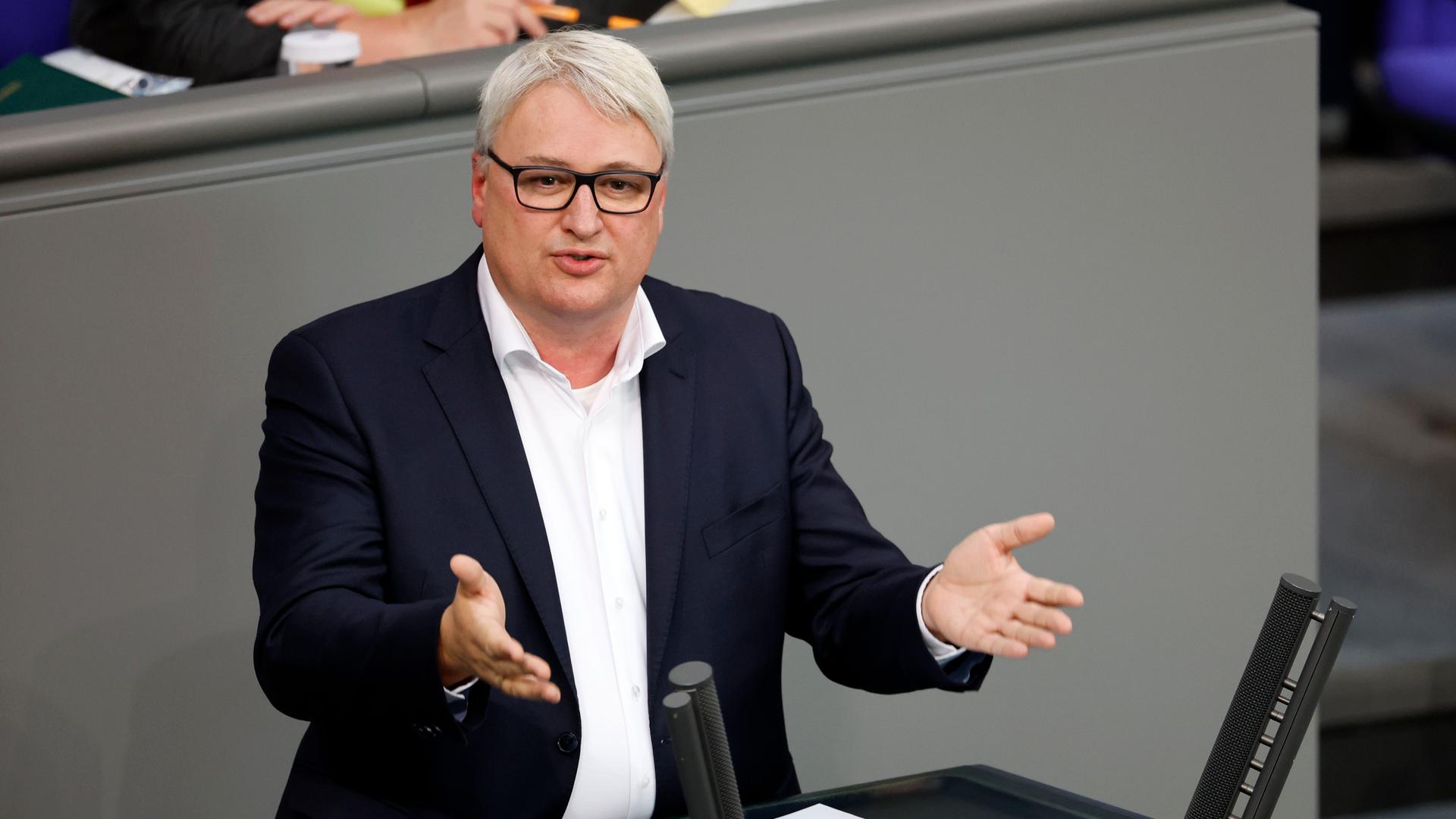 Rix trägt einen Anzug ohne Krawatte. Er steht am Rednerpult im Bundestag, spricht und gestikuliert mit beiden Händen.