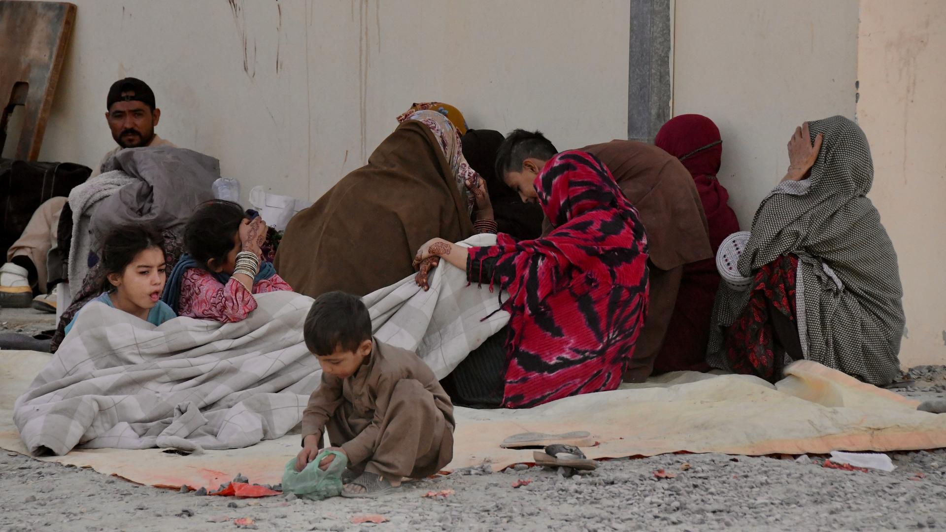 Aus Pakistan in die Provinz Kandahar zurückgekehrte afghanische Flüchtlinge sitzen auf dem Boden vor einer Häuserwand.