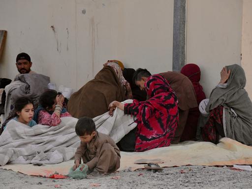 Aus Pakistan in die Provinz Kandahar zurückgekehrte afghanische Flüchtlinge sitzen auf dem Boden vor einer Häuserwand.