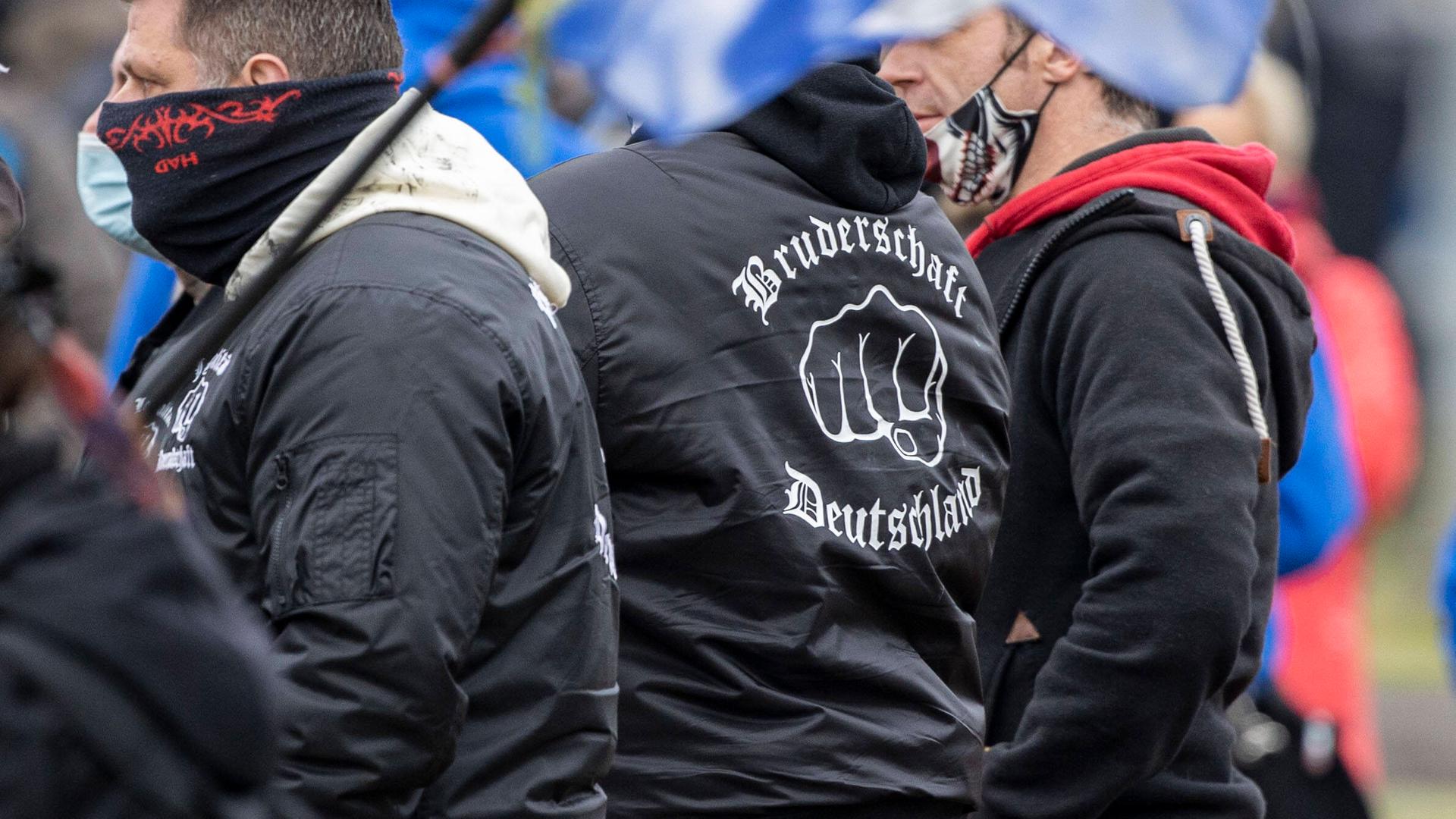 Rechtsextreme bei einer Querdenker-Demo. Einer trägt eine Jacke mit der Aufschrift Bruderschaft Deutschland.