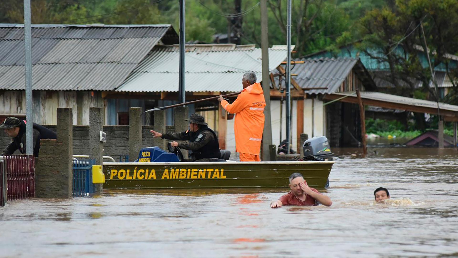 Polizeibeamte kontrollieren ein Haus, während Anwohner über eine überschwemmte Straße im Bundesstaat Rio Grande do Sul waten.