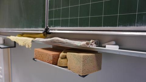 Unter einer Tafel an einer allgemeinbildenden Schule sind Tafelschwämme und Kreide zu sehen.