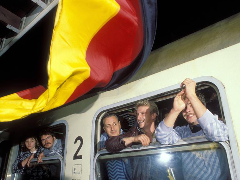 DDR-Flüchtlinge im Zug während der Ankunft in Hof im Oktober 1989. Vor dem Zug weht eine bundesdeutsche Flagge.