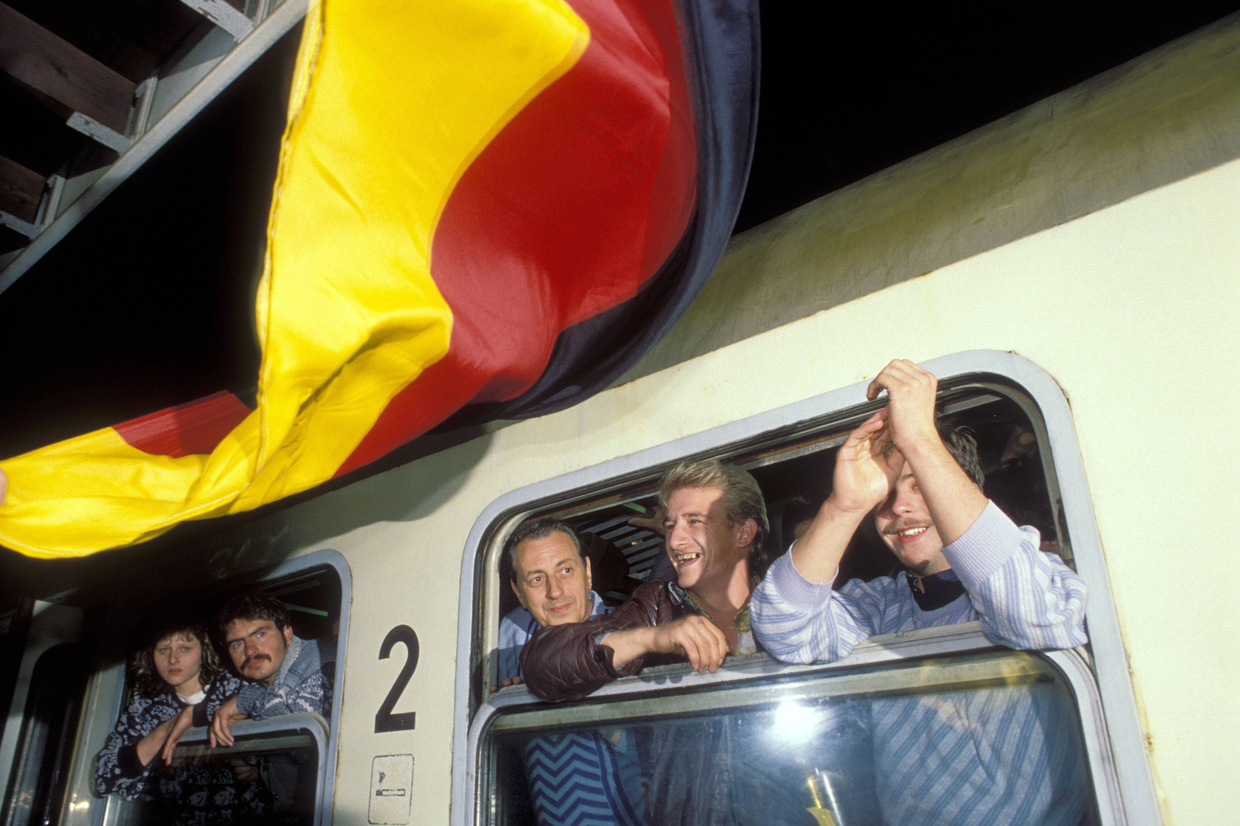 DDR-Flüchtlinge im Zug während der Ankunft in Hof im Oktober 1989. Vor dem Zug weht eine bundesdeutsche Flagge.