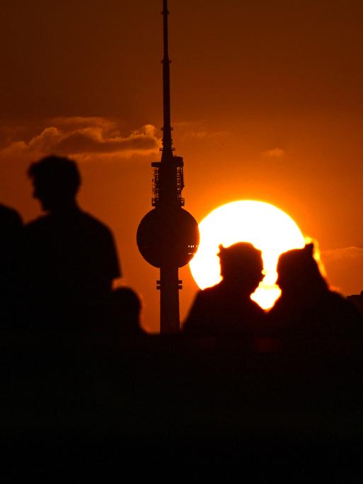 Silhouetten von Personen und dem Berliner Fernsehturm vor einem Sonnenuntergang.