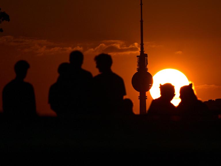 Silhouetten von Personen und dem Berliner Fernsehturm vor einem Sonnenuntergang.