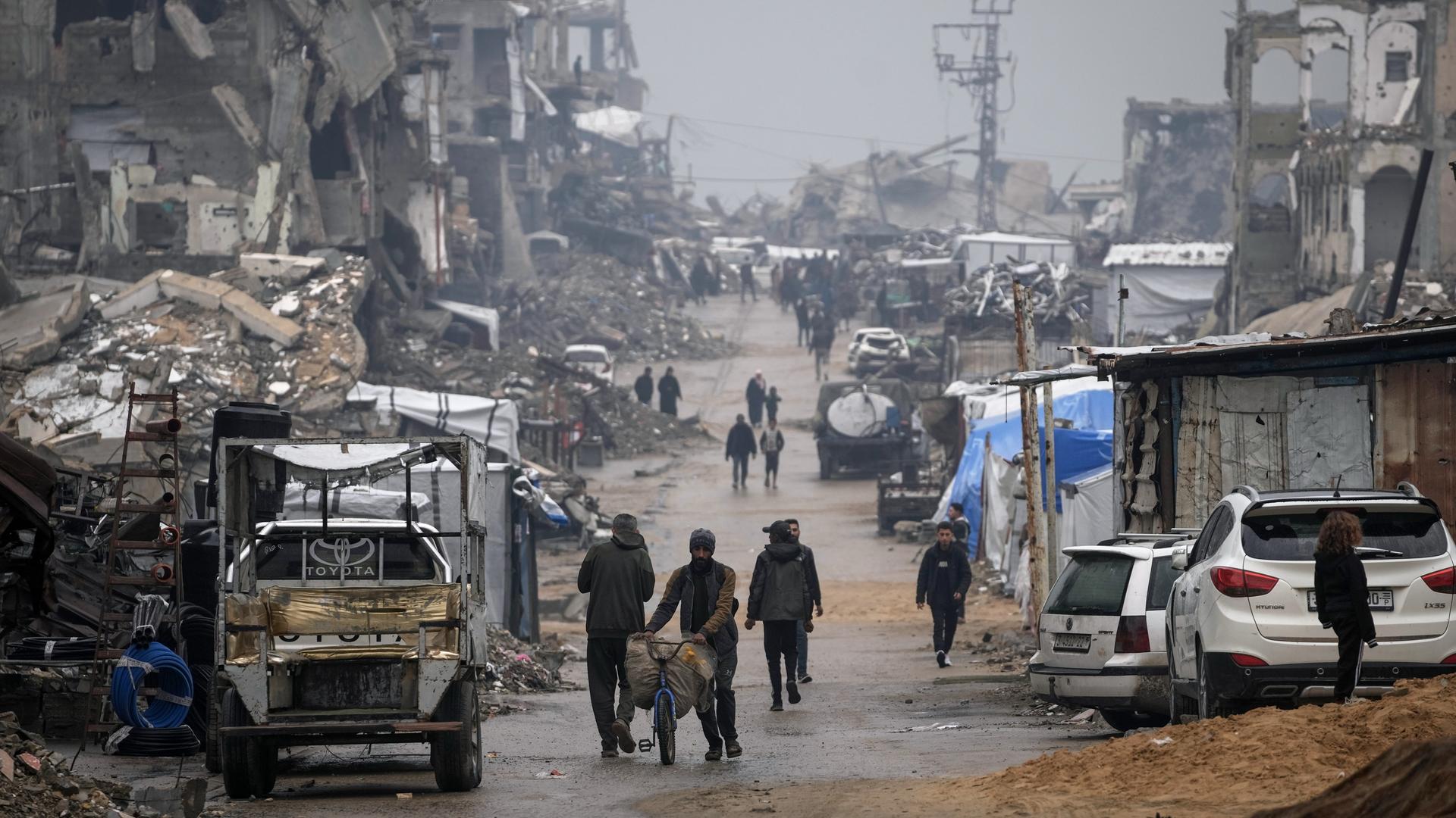 Palästinenser gehen im Regen eine Straße mit kriegszerstörten Gebäuden in Gaza entlang. Palästinenser gehen im Regen eine Straße mit kriegszerstörten Gebäuden in Gaza entlang.