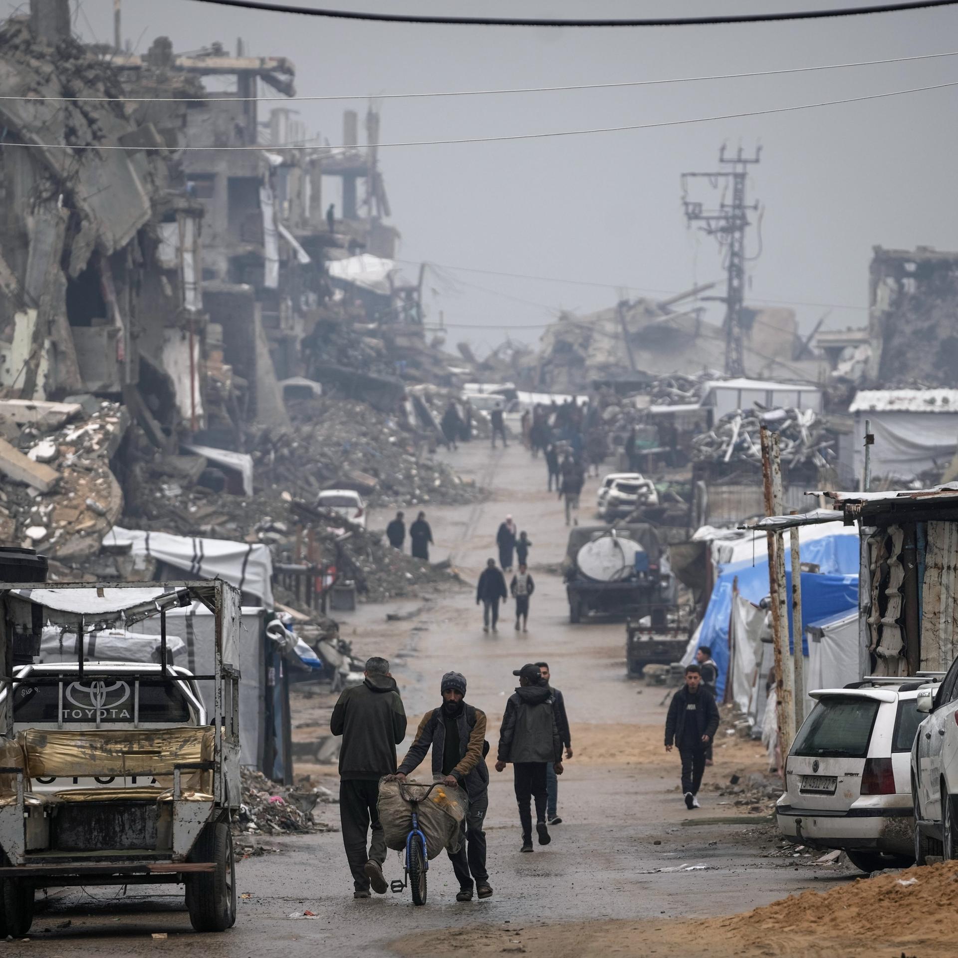 Palästinenser gehen im Regen eine Straße mit kriegszerstörten Gebäuden in Gaza entlang.