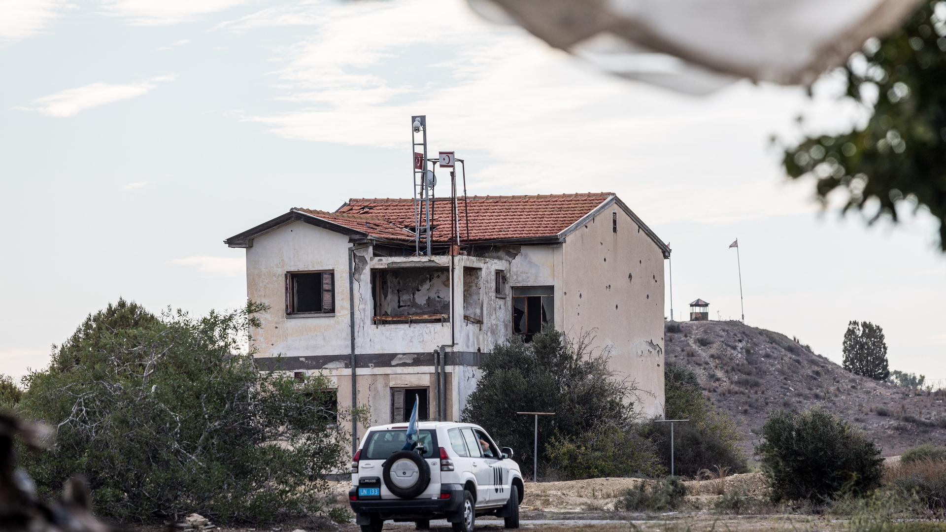 Ein UN Fahrzeug passiert eine verlassenes Haus innerhalb der Pufferzone. Die türkische Armee installierte die Flagge der Türkei und der so genannten "Türkischen Republik Nordzypern" auf dem Dach eines verlassenen Hauses, das als "Haus von Christalla" bekannt wurde.