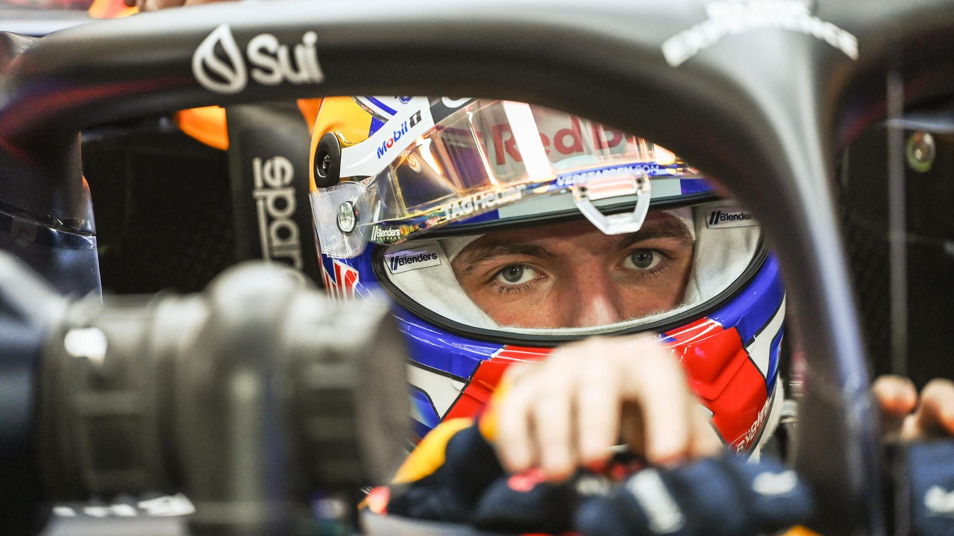 Max Verstappen in seinem Rennauto von Red Bull mit Helm auf. Er schaut direkt in die Kamera.