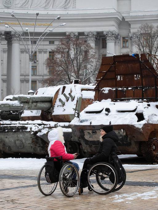Frauen in Rollstühlen unterhalten sich in der Nähe von zerstörten russischen Panzern im Zentrum von Kiew