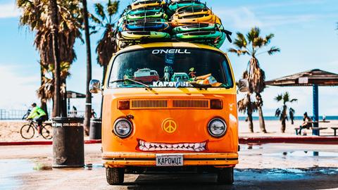 Ein orangfarbener VW Bus mit Surfboards auf dem Dach und einem Peace-Zeichen anstelle des VW-Emblems. Ein orangfarbener VW Bus mit Surfboards auf dem Dach und einem Peace-Zeichen anstelle des VW-Emblems.