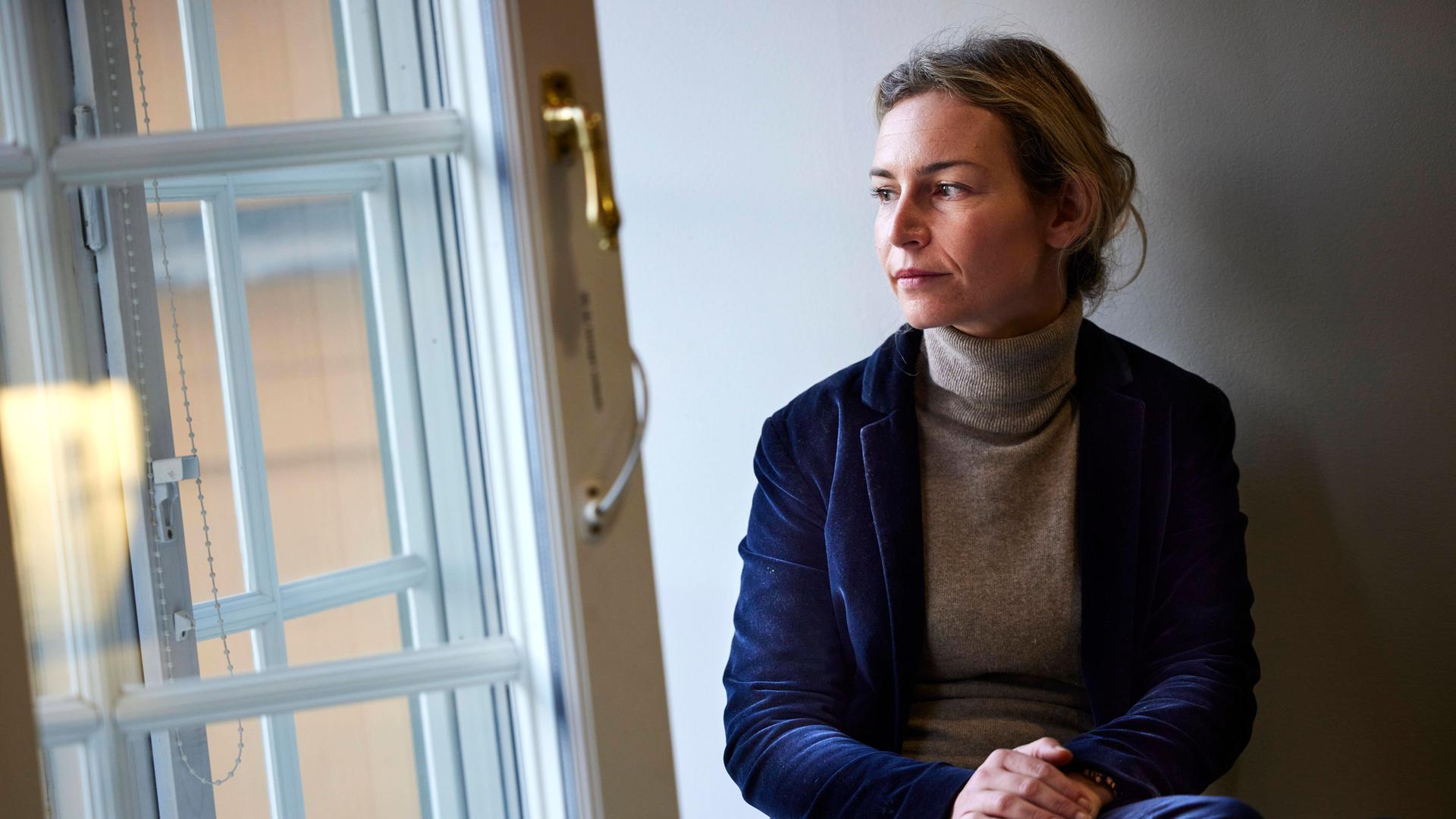 Die albanische Autorin Lea Ypi sitzt mit überschlagenen Beinen an einem geöffneten Fenster und blickt nach draußen.