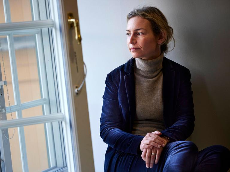 Die albanische Autorin Lea Ypi sitzt mit überschlagenen Beinen an einem geöffneten Fenster und blickt nach draußen.