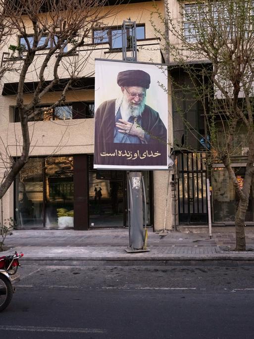 Ein Motorrad fährt in Teheran an einem Plakat mit dem Bild des getöteten iranischen Obersten Führers Chamenei vorbei. 
