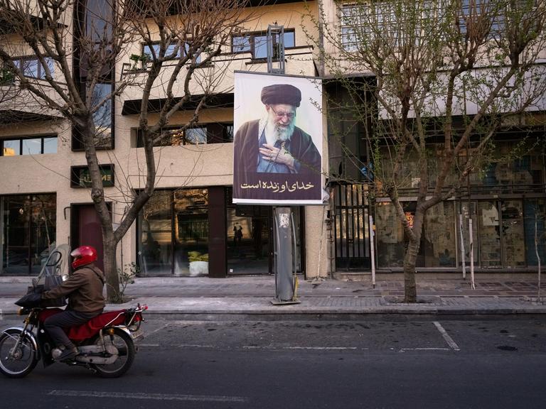 Ein Motorrad fährt in Teheran an einem Plakat mit dem Bild des getöteten iranischen Obersten Führers Chamenei vorbei. 
