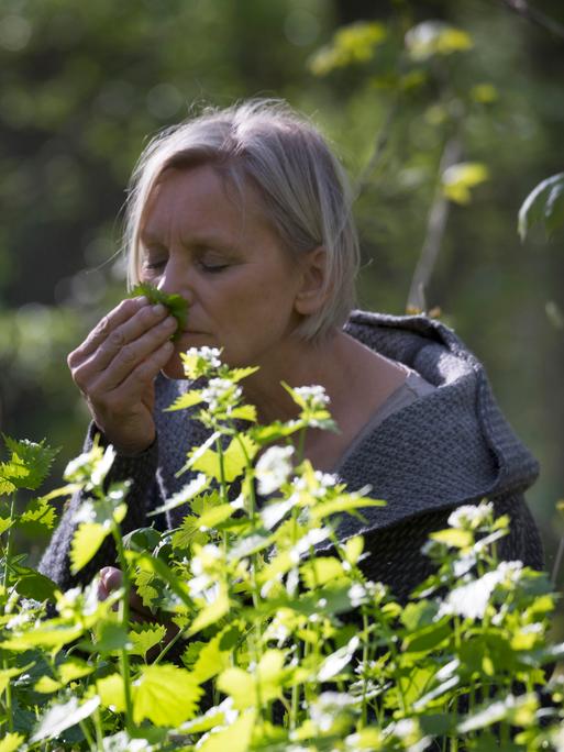 Eine Frau riecht an einer Knoblauchrauke. 