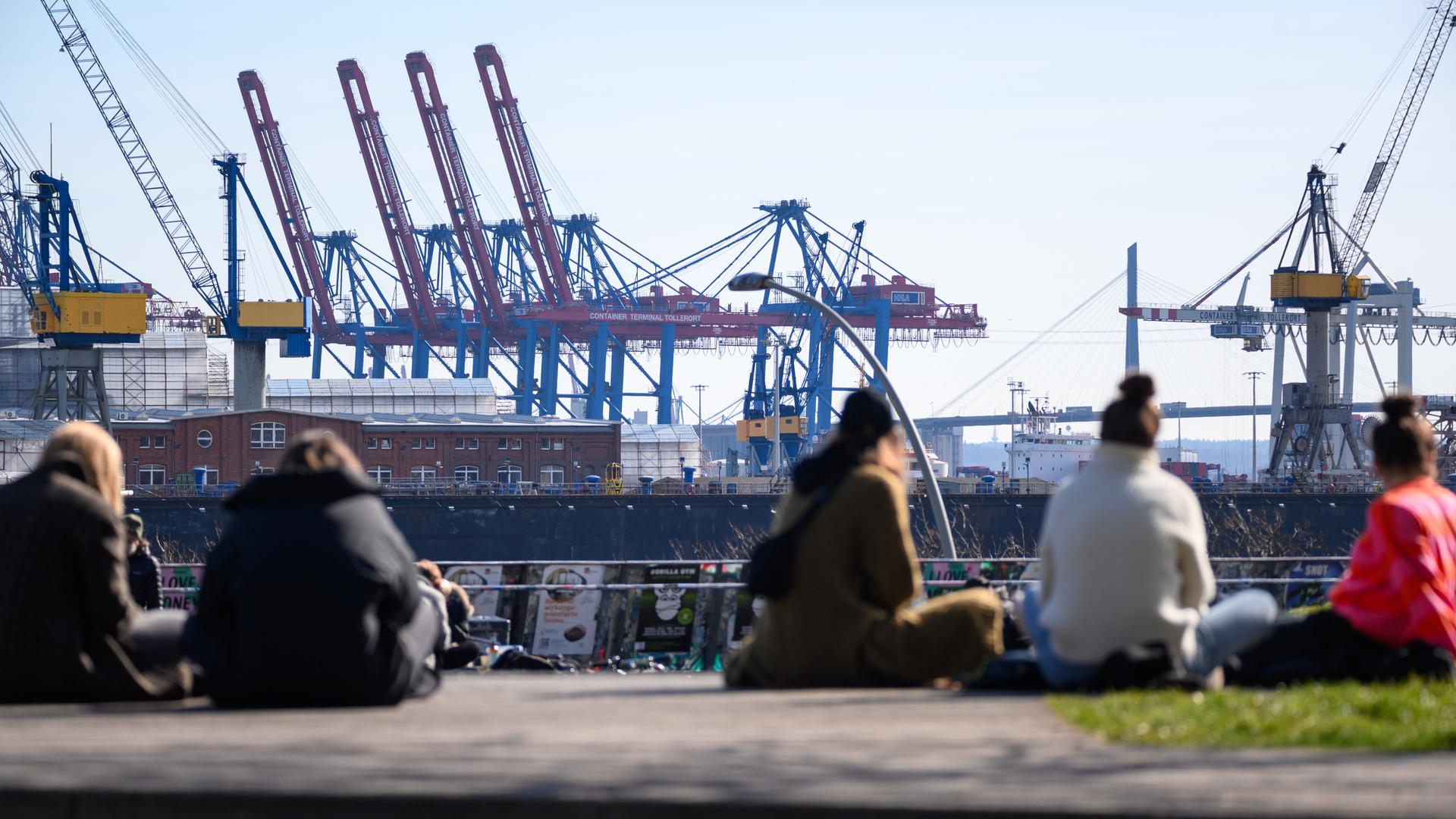Passanten sitzen im Sonnenschein im Park Fiction auf St. Pauli gegenüber zahlreichen Hafenkränen und Docks. Passanten sitzen im Sonnenschein im Park Fiction auf St. Pauli gegenüber zahlreichen Hafenkränen und Docks.