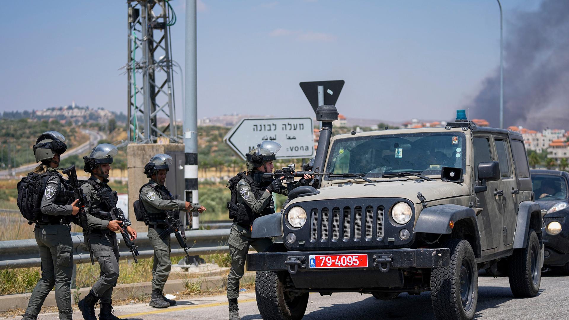 Israelische Grenzpolizisten kontrollieren Autos auf der Hauptstraße zur Stadt Turmus Ayya. Im Hintergrund ist eine große Rauchwolke zu sehen.