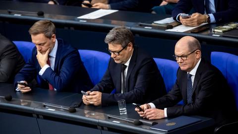 Bundeskanzler Olaf Scholz, Bundeswirtschaftsminister Robert Habeck und Bundesfinanzminister Christian Lindner (v.r.) schauen nebeneinander sitzend in ihre Handys.