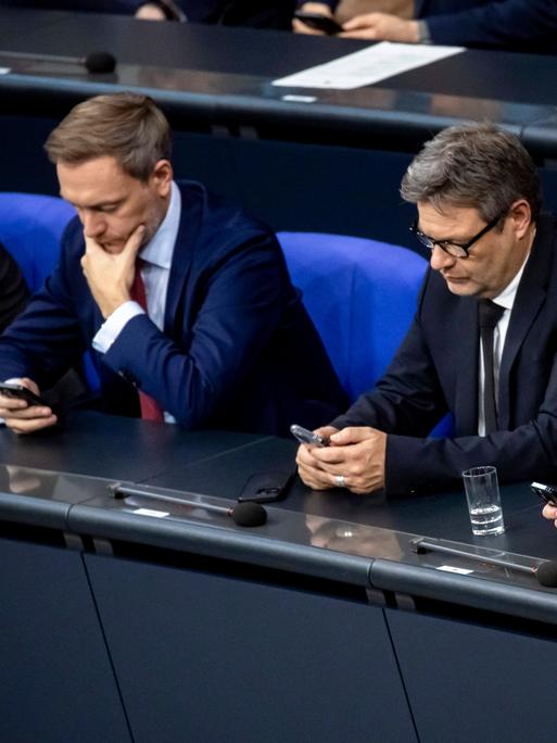 Bundeskanzler Olaf Scholz, Bundeswirtschaftsminister Robert Habeck und Bundesfinanzminister Christian Lindner (v.r.) schauen nebeneinander sitzend in ihre Handys.