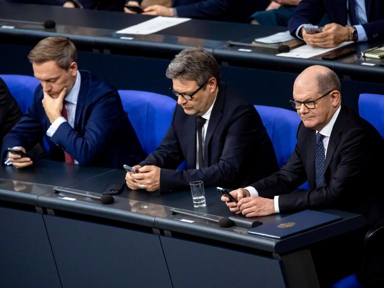 Bundeskanzler Olaf Scholz, Bundeswirtschaftsminister Robert Habeck und Bundesfinanzminister Christian Lindner (v.r.) schauen nebeneinander sitzend in ihre Handys.