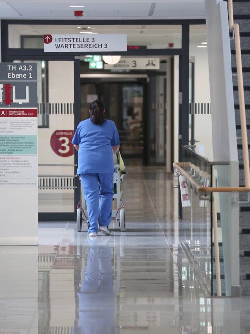 Eine Pflegekraft in blauer Pflegekleidung schiebt eine Person in einem Rollstuhl im Universitären Notfallzentrum in der Hanse- und Universitätsstadt Rostock.