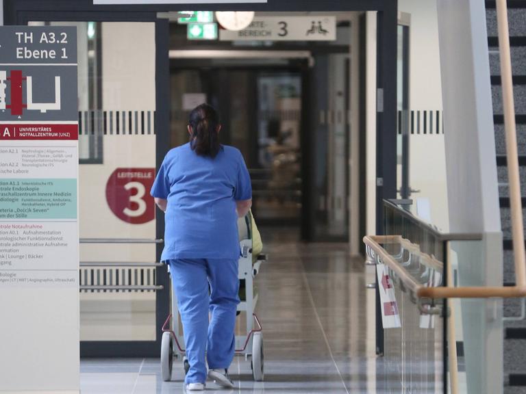 Eine Pflegekraft in blauer Pflegekleidung schiebt eine Person in einem Rollstuhl im Universitären Notfallzentrum in der Hanse- und Universitätsstadt Rostock.