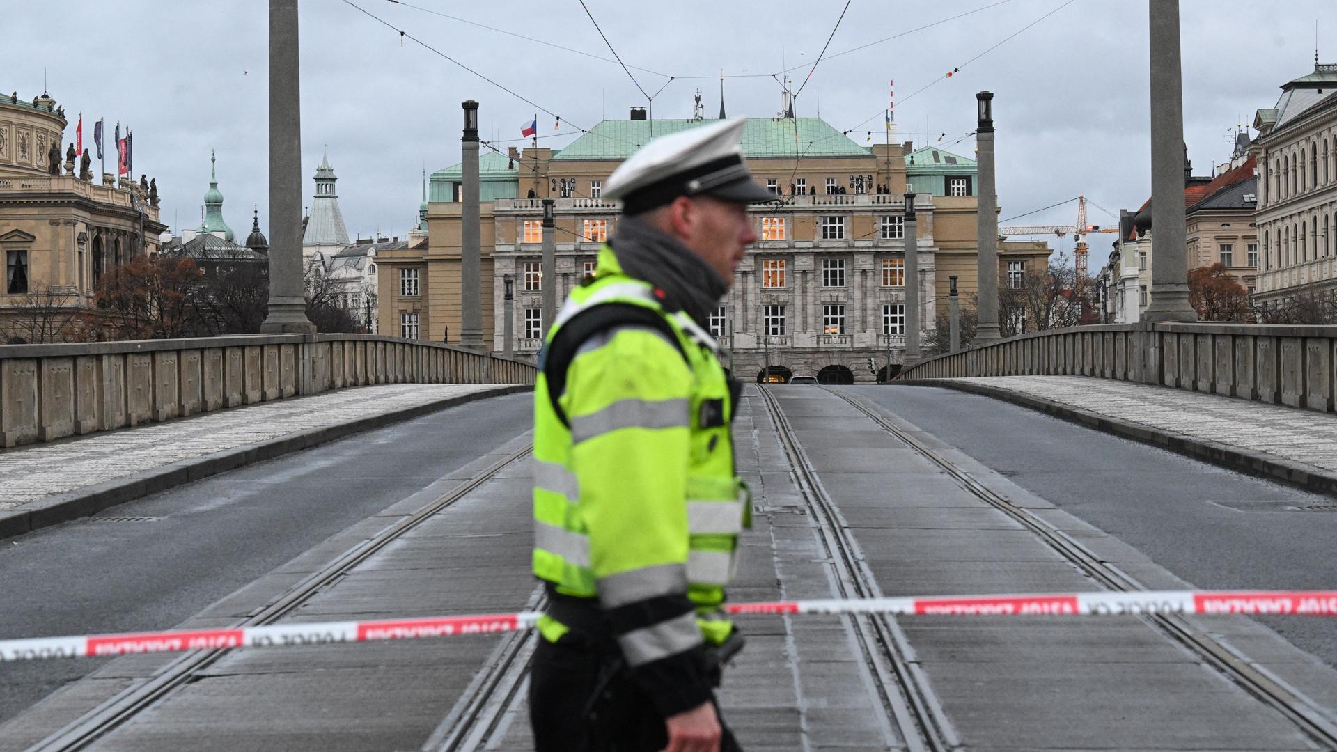 Ein Polizist in gelber Warnweste spannt eine Absperrung über eine Straße. Im Hintergrund das Universitätsgebäude.