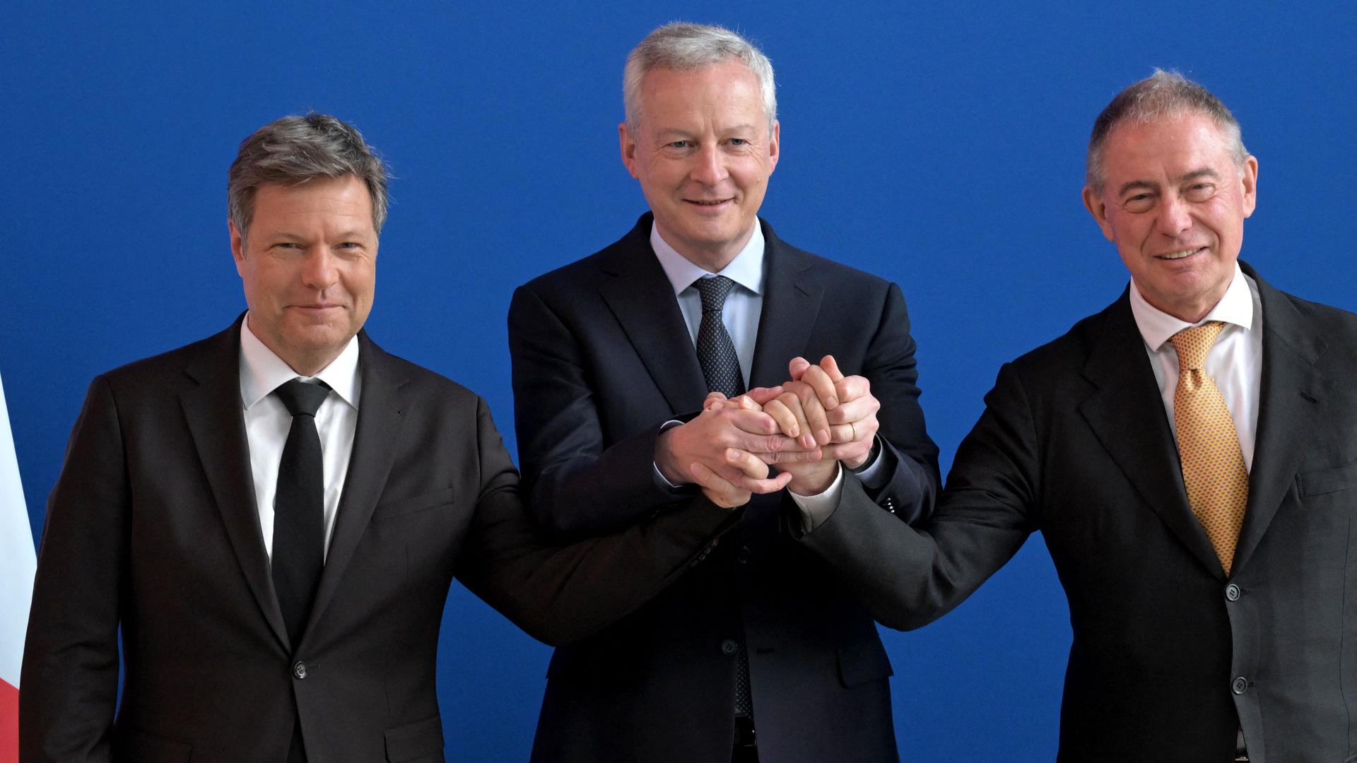 Robert Habeck, Bruno Le Maire und Adolfo Urso stehen nebeneinander und reichen einander die Hände.